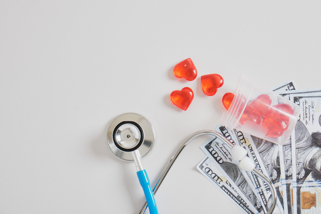 money, hearts in a jar for analyzes and a medical stethoscope on a gray background copy space, sperm and egg donation, artificial insemination and surrogacy concept, dollar bills