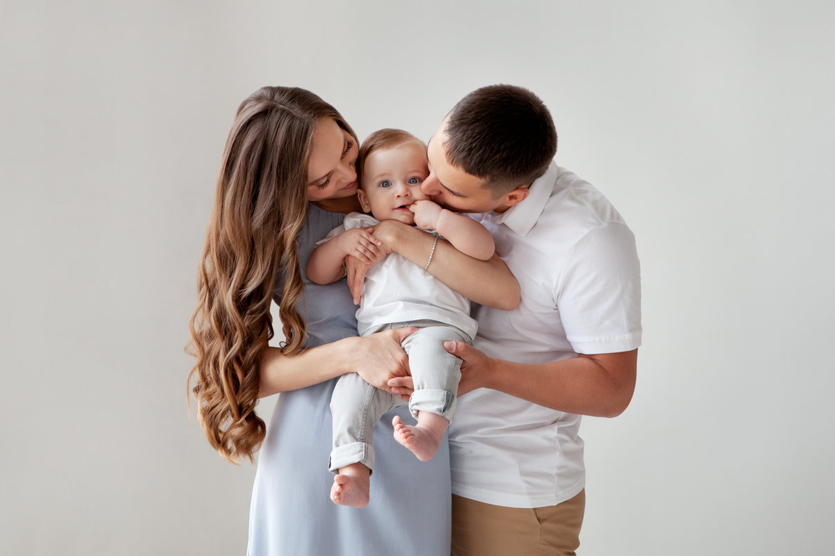 Happy young family. Beautiful Mother and father kissing their baby . Parents, Portrait of Mom, dad and smiling child on hands isolated over white background.