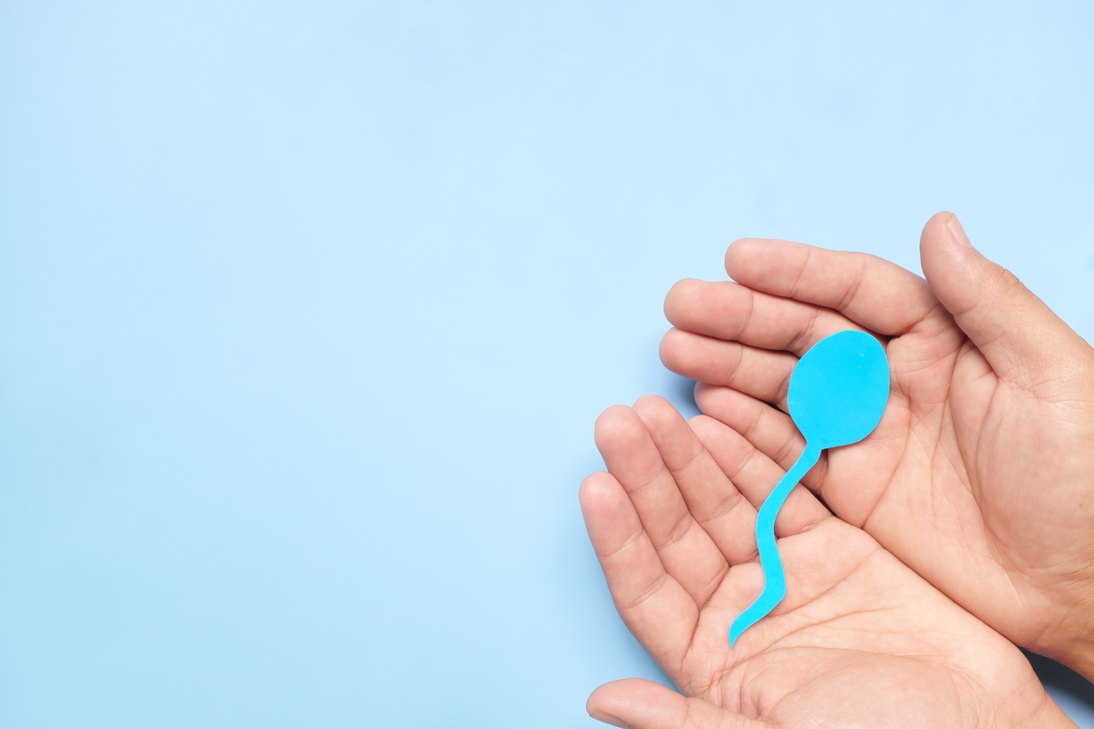 Top view of male hand holding sperm cutout in blue background. Men's health, sperm donation and care concept.