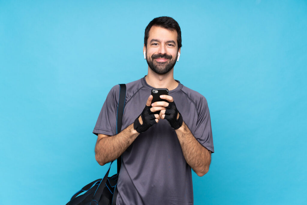 Young sport man with beard over isolated blue background sending a message with the mobile