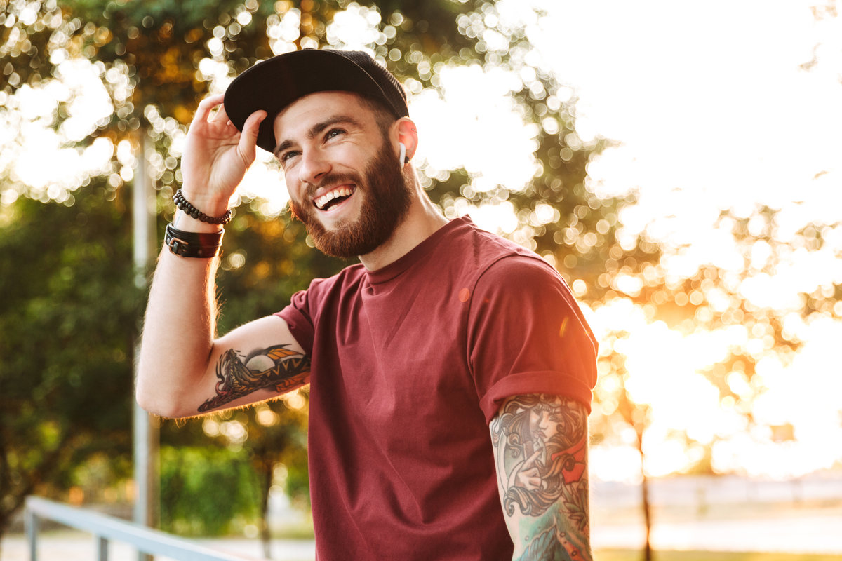 Handsome young man dressed in casual clothing walking at the park, listening to music with wireless earphones