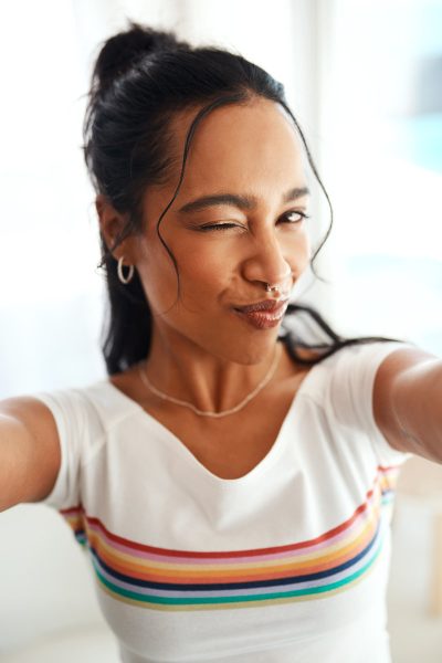 Woman, portrait and wink selfie for profile picture, vlog or social media post at home. Happy, influencer or creative vlogger in POV with casual fashion, photo or memory in living room with smile.