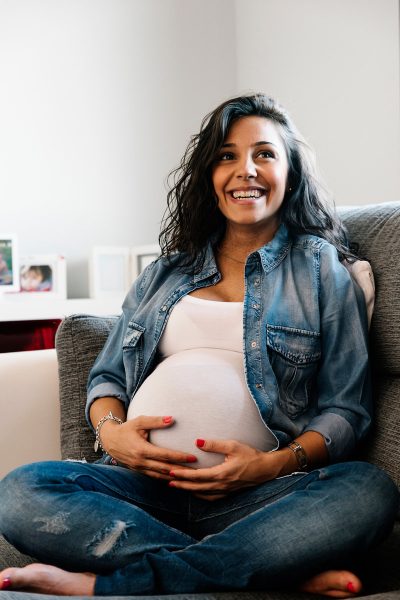 Pretty Pregnant woman sitting on a sofa at home.