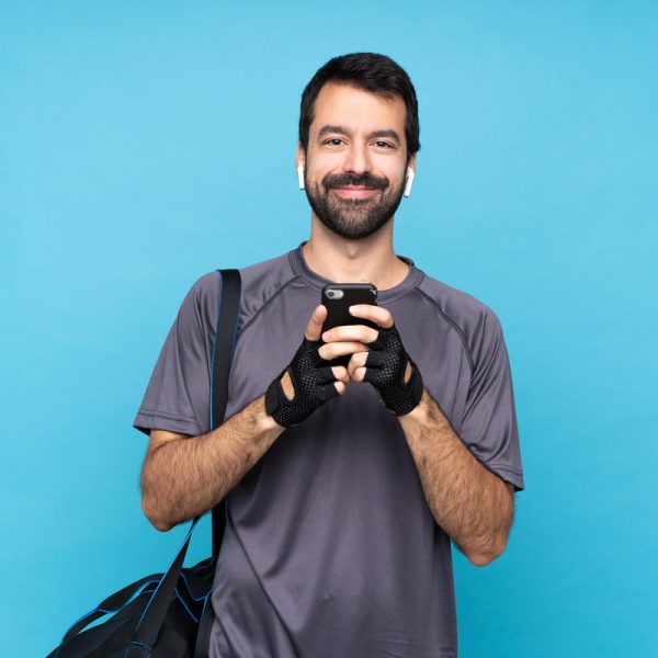 Young sport man with beard over isolated blue background sending a message with the mobile