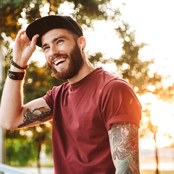 Handsome young man dressed in casual clothing walking at the park, listening to music with wireless earphones