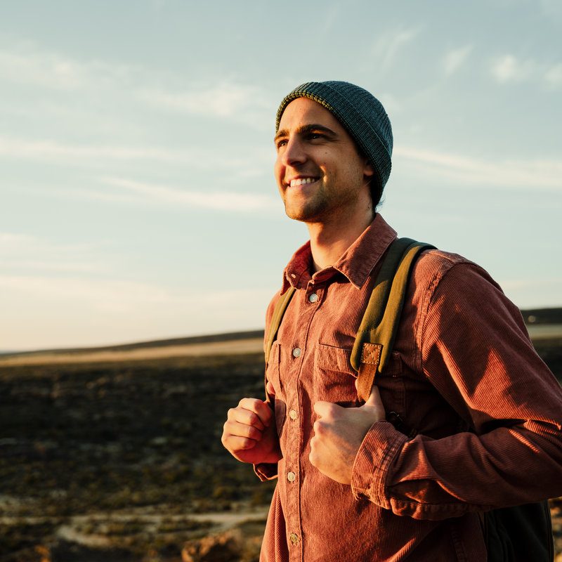 Caucasian male hiker walking with backpack through wilderness embracing sunrise while enjoying nature. High quality photo