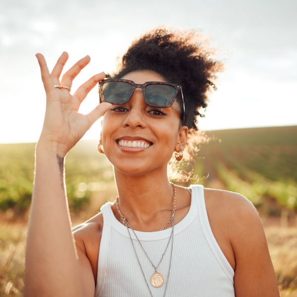 Young black woman, sunset portrait in field countryside and happy smile with summer sunglasses in Brazil. Outdoor adventure in nature, travel freedom on vacation and holiday .trip alone in sunshine.